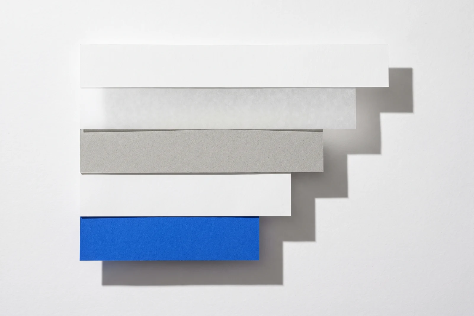Des pièces de papier vierge disposées en escalier descendant, ombres dures projetées vers le bas à droite.