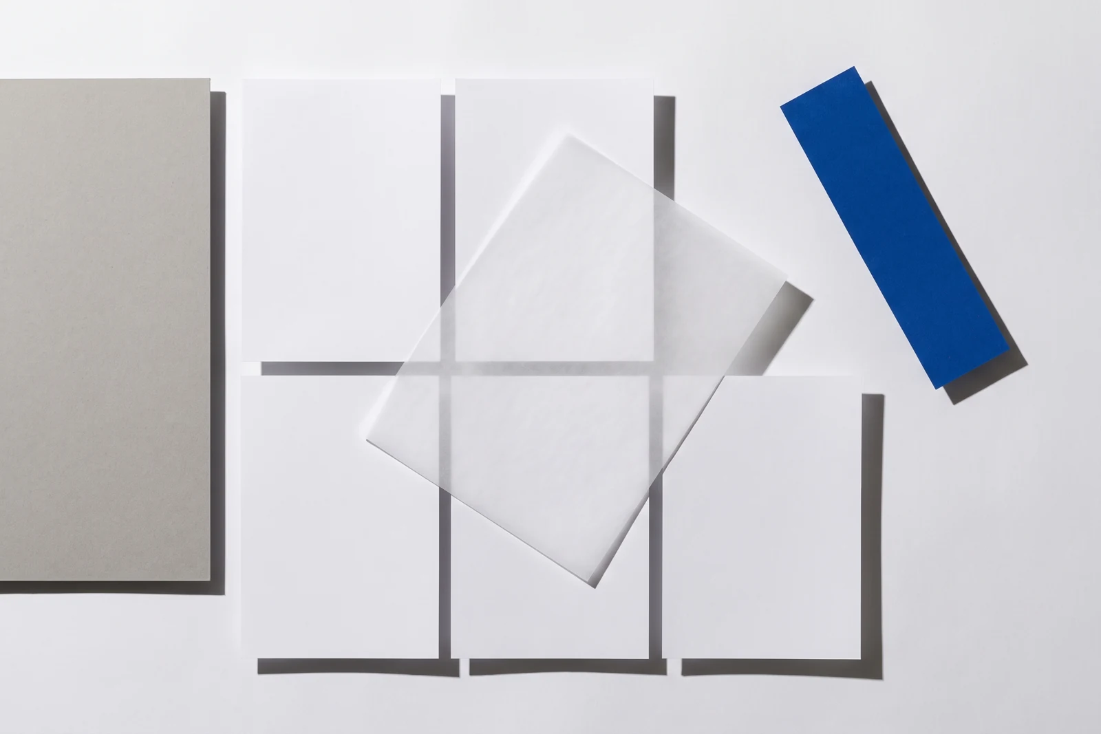 Un calque cristal posé de biais sur des feuilles de papier vierge, ombres dures projetées vers le bas à droite.