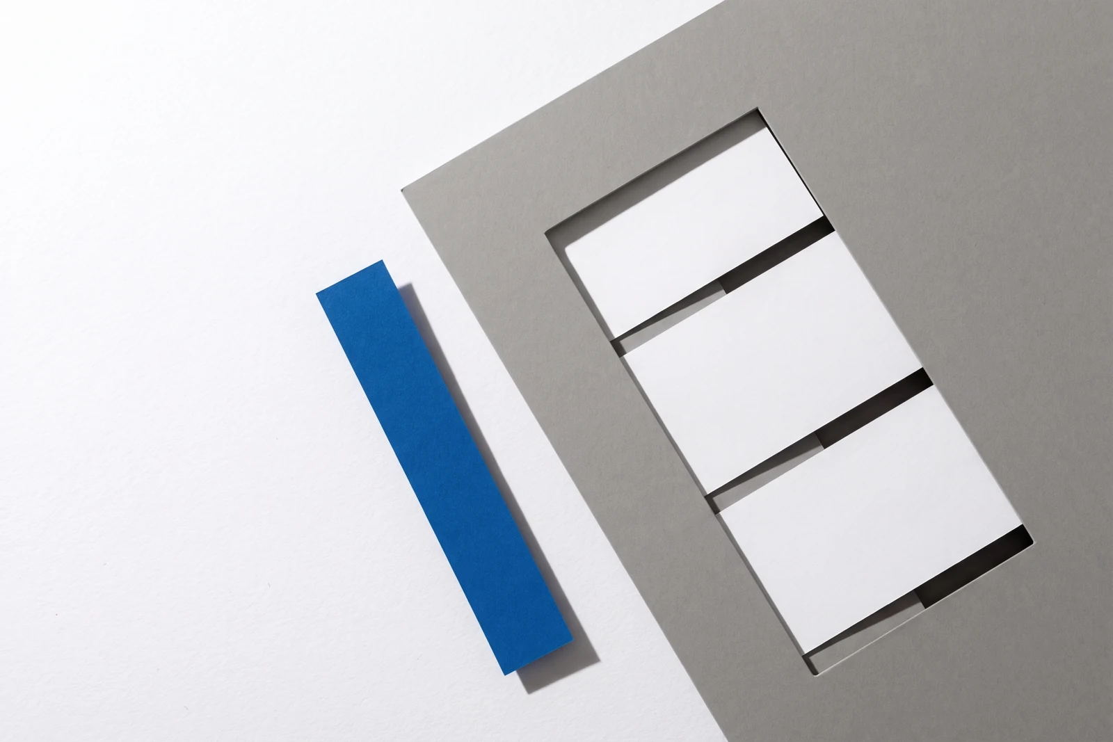 Une fenêtre rectangulaire découpée dans une plaque de carton gris laisse voir des cartes dessous, ombres dures projetées vers le bas à droite.