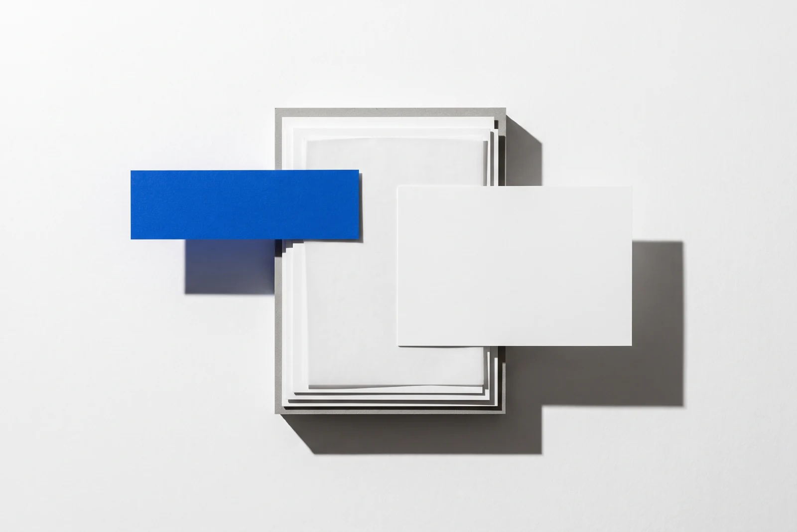 Une carte glissée hors d’une pile de papier vierge et qui dépasse nettement, ombres dures projetées vers le bas à droite.