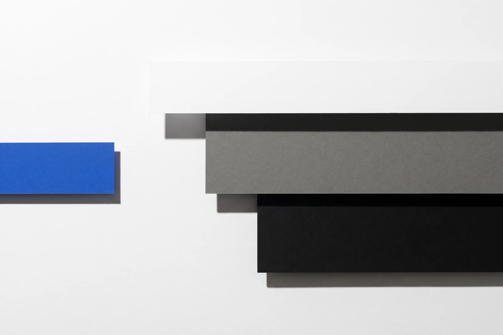 Des pièces de papier vierge disposées en escalier descendant, ombres dures projetées vers le bas à droite.