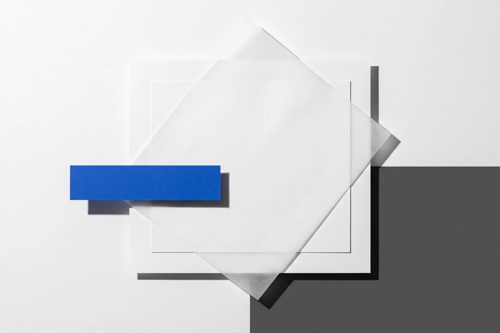 Un calque cristal posé de biais sur des feuilles de papier vierge, ombres dures projetées vers le bas à droite.