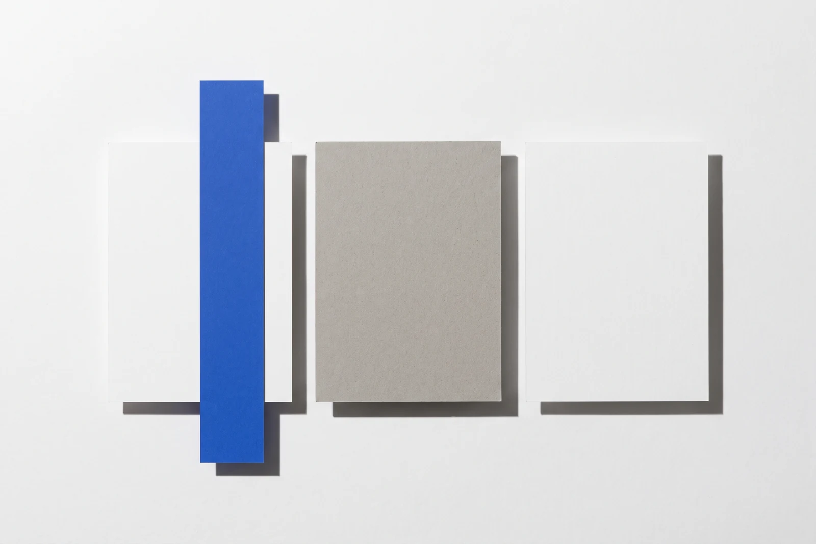 Une plaque de carton gris posée à plat masque le centre d’une rangée de cartes, ombres dures projetées vers le bas à droite.