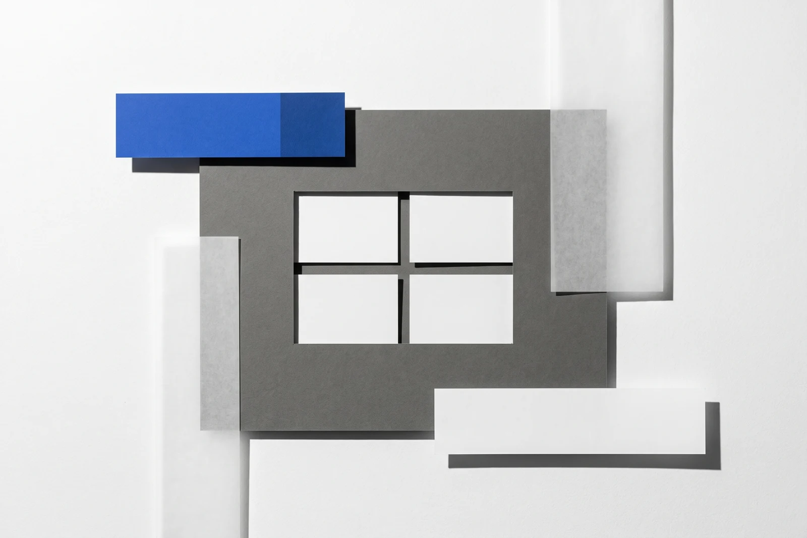 Une fenêtre rectangulaire découpée dans une plaque de carton gris laisse voir des cartes dessous, ombres dures projetées vers le bas à droite.