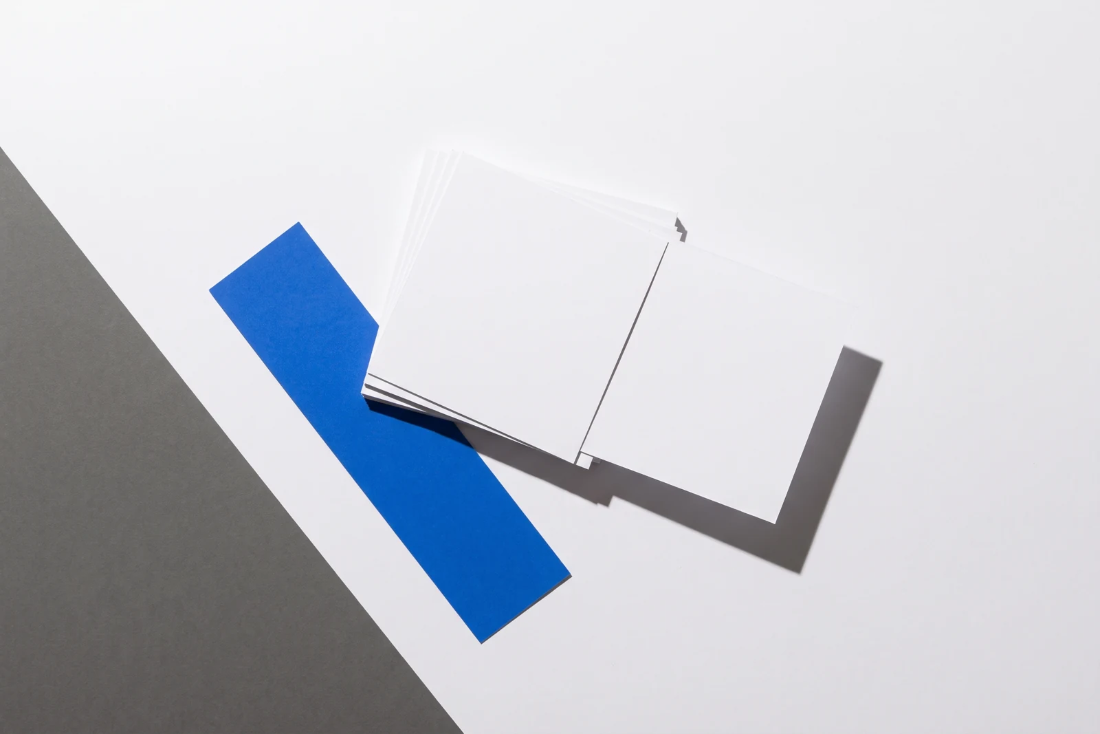 Une carte glissée hors d’une pile de papier vierge et qui dépasse nettement, ombres dures projetées vers le bas à droite.