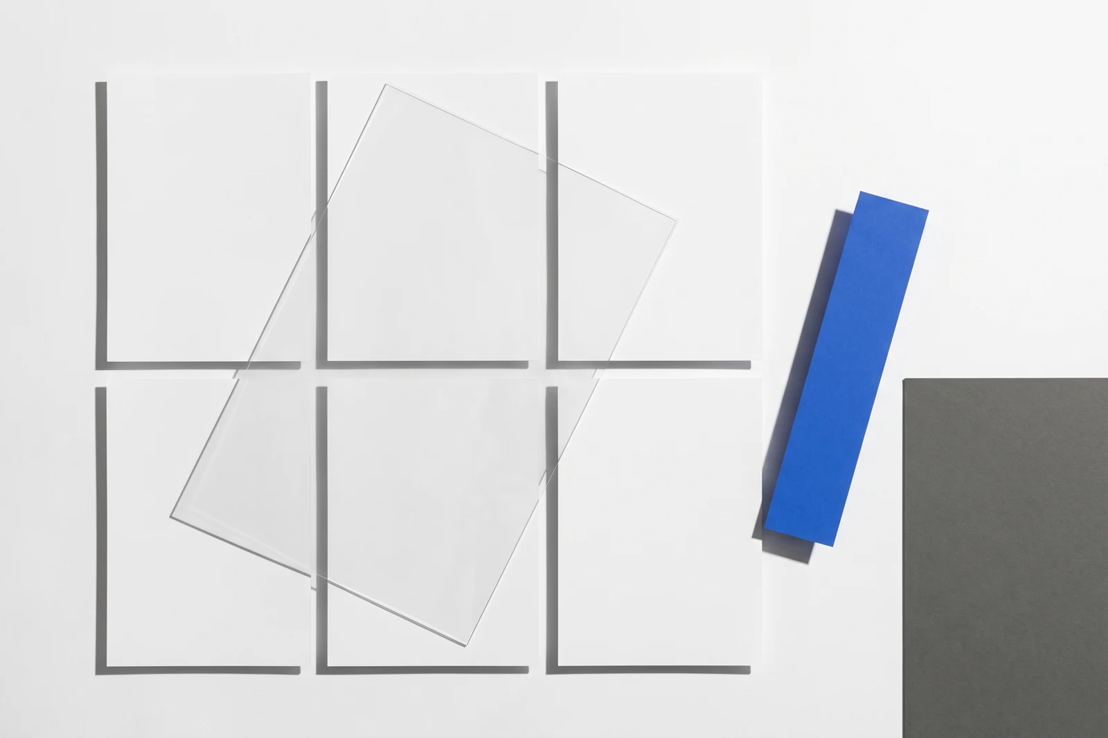 Un calque cristal posé de biais sur des feuilles de papier vierge, ombres dures projetées vers le bas à droite.