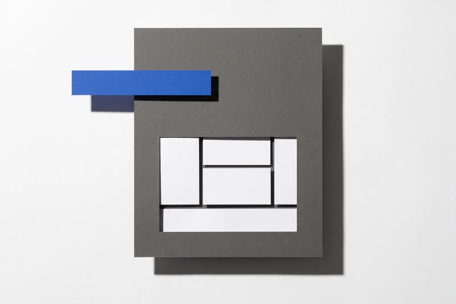 Une fenêtre rectangulaire découpée dans une plaque de carton gris laisse voir des cartes dessous, ombres dures projetées vers le bas à droite.