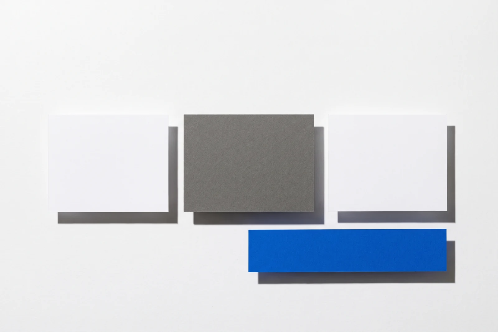 Une plaque de carton gris posée à plat masque le centre d’une rangée de cartes, ombres dures projetées vers le bas à droite.