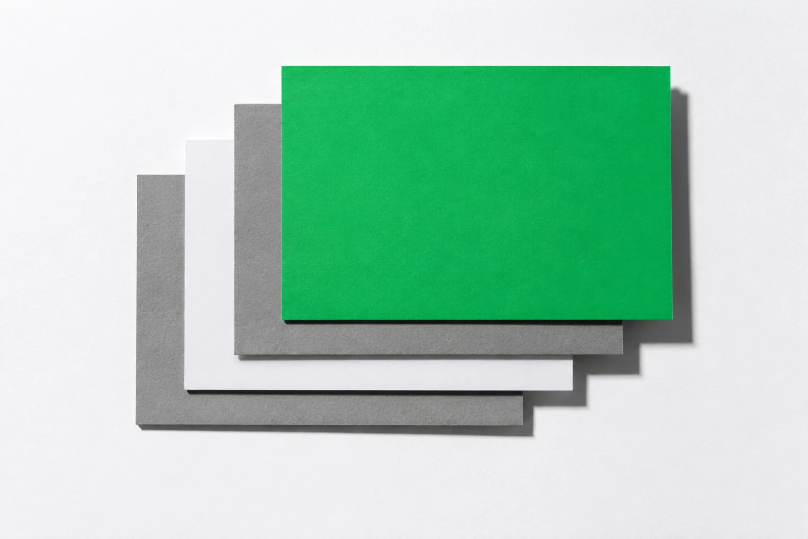 Quatre feuilles de carton gris, de papier blanc et de papier vert posées en escalier, la feuille verte au sommet.