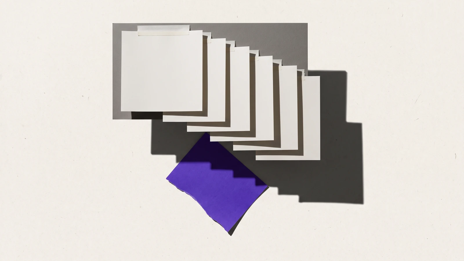 Des feuilles de papier fin collées en couches qui se recouvrent partiellement, ombres dures projetées vers le bas à droite.