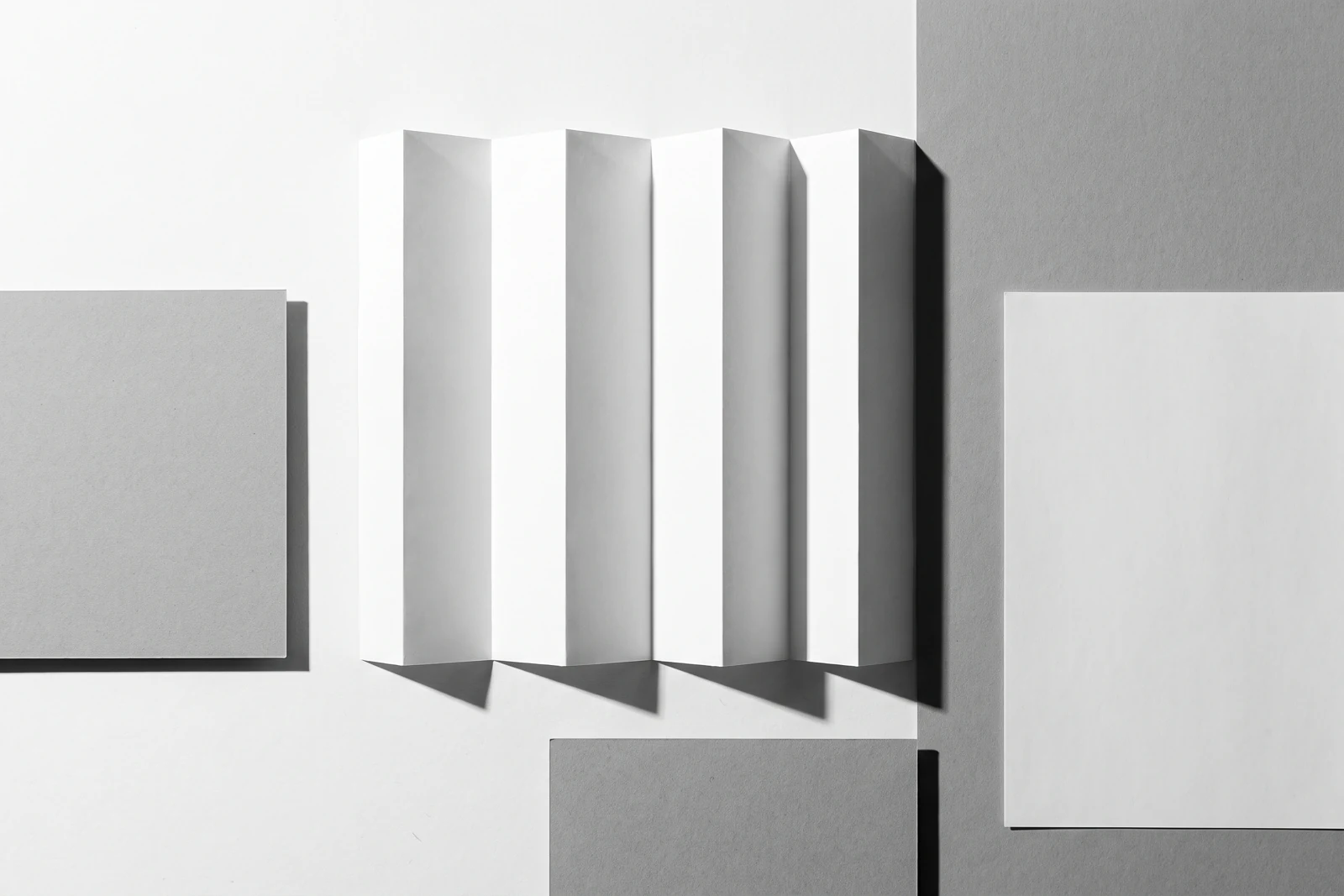 Une feuille de papier fin pliée en accordéon à arêtes vives, ombres dures projetées vers le bas à droite.