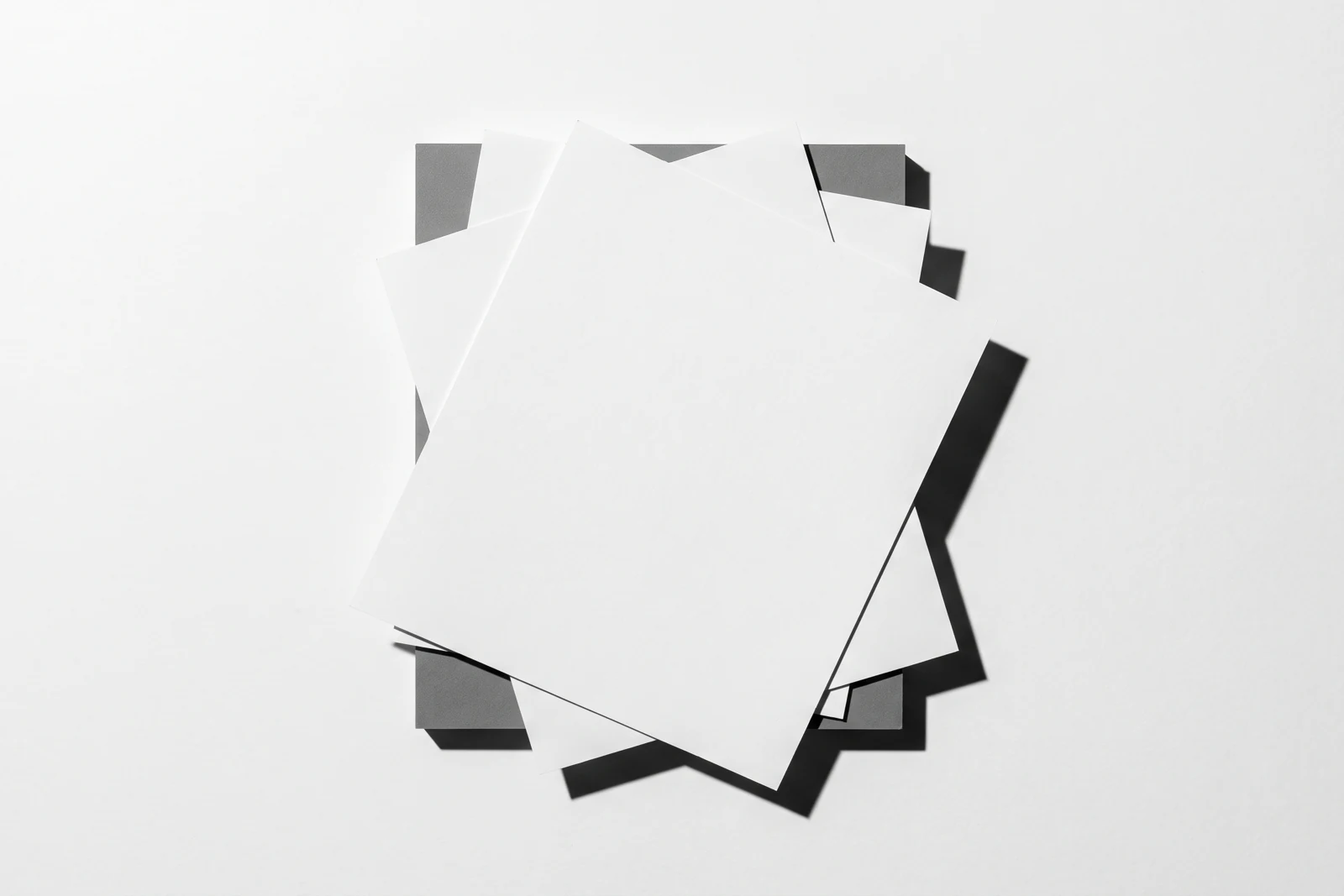 Des feuilles de papier fin empilées à plat et visiblement désalignées, ombres dures projetées vers le bas à droite.