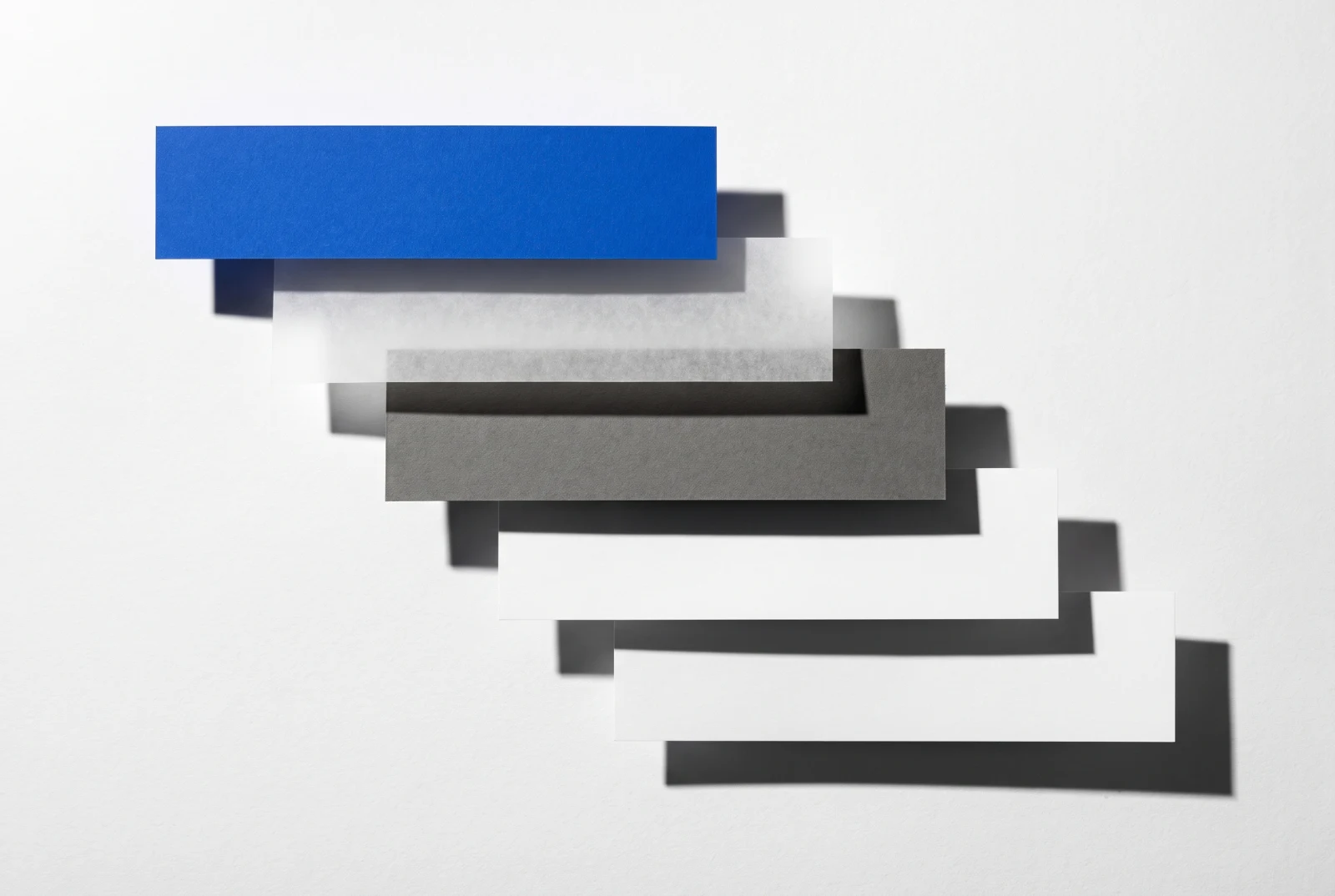 Des pièces de papier vierge disposées en escalier descendant, ombres dures projetées vers le bas à droite.